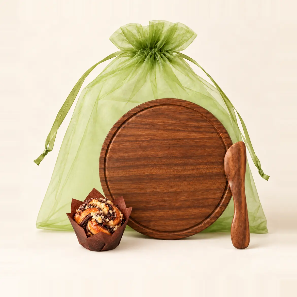 A round wooden board and a wooden knife in front of a green organza gift bag, with a mini chocolate babka beside them.